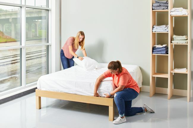 to kvinner som lager seng med hvite laken