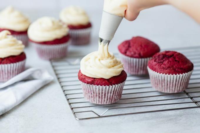 Piping kremost frosting på rød fløyel cupcakes.